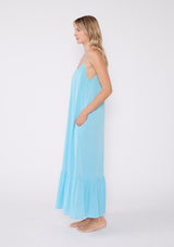 [Color: Aqua] A side facing image of a blonde model wearing an aqua blue bohemian sleeveless maxi dress. With spaghetti straps, a scoop neckline, side pockets, a long flowy tiered skirt, and a sheer lace racerback detail.
