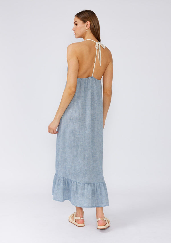 [Color: Dusty Blue] A back facing image of a brunette model wearing a dusty blue bohemian halter beach dress designed in soft cotton gauze. With a v neckline, a long tiered skirt with front slit, an adjustable rope halter tie neckline, and a t back strap detail. 