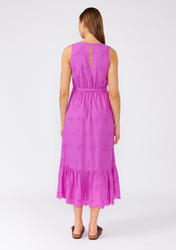 [Color: Orchid] A back facing image of a brunette model wearing a an orchid purple bohemian mid length dress made with embroidered eyelet. A sleeveless spring dress with a v neckline, a tiered skirt, an adjustable waist tie, and a back keyhole with button closure. 