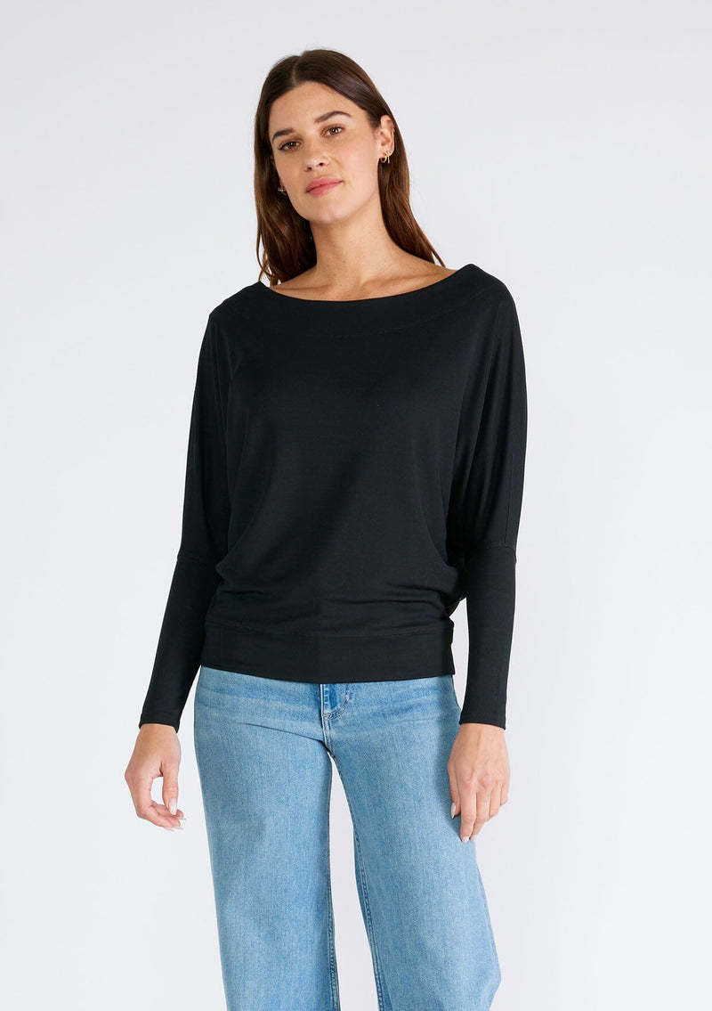 [Color: Black] A front facing image of a brunette model wearing a black soft ribbed knit pullover. With long dolman sleeves and a wide boat neck that can be worn on or off the shoulder. 
