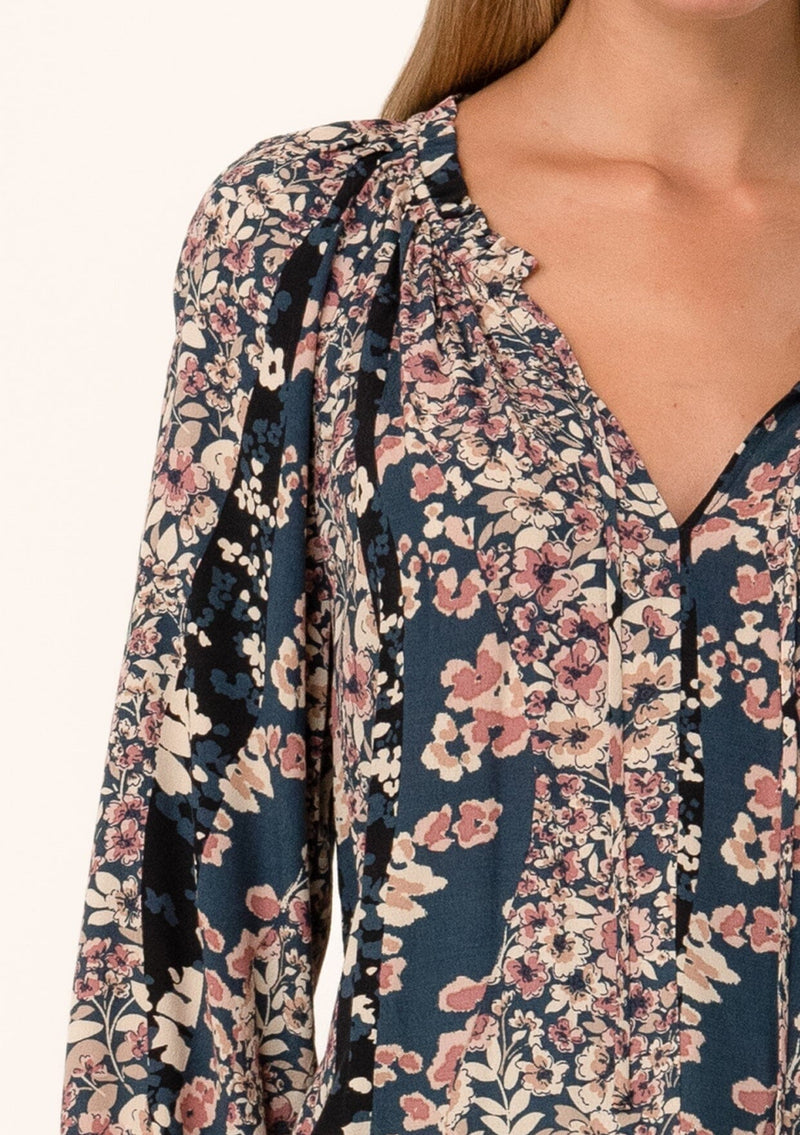[Color: Dusty Rose/Navy] A close up front facing image of a blonde model wearing a bohemian fall blouse in a mixed blue and pink floral print. With voluminous long sleeves, smocked elastic wrist cuffs, a split v neckline with ties, and a relaxed fit. 