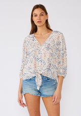 [Color: Cream/Dusty Blue] A front facing image of a brunette model wearing a lightweight bohemian blouse designed in an off white and blue print. With a v neckline, a tie waist detail, and three quarter length sleeves. 