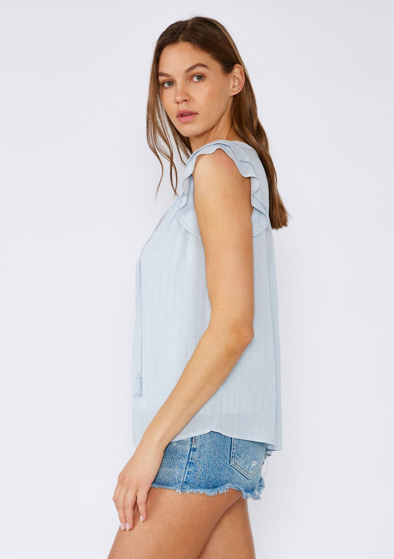 [Color: Periwinkle] A side facing image of a brunette model wearing a light blue bohemian spring top with gold metallic thread details. Featuring short double flutter sleeves, a v neckline with tassel ties, and a relaxed fit. 