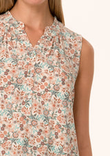[Color: Cream/Teal] A close up front facing image of a blonde model wearing a transitional fall sleeveless blouse in a cream and teal floral print. With a button front, a ruffle trimmed neckline, and a relaxed fit. 