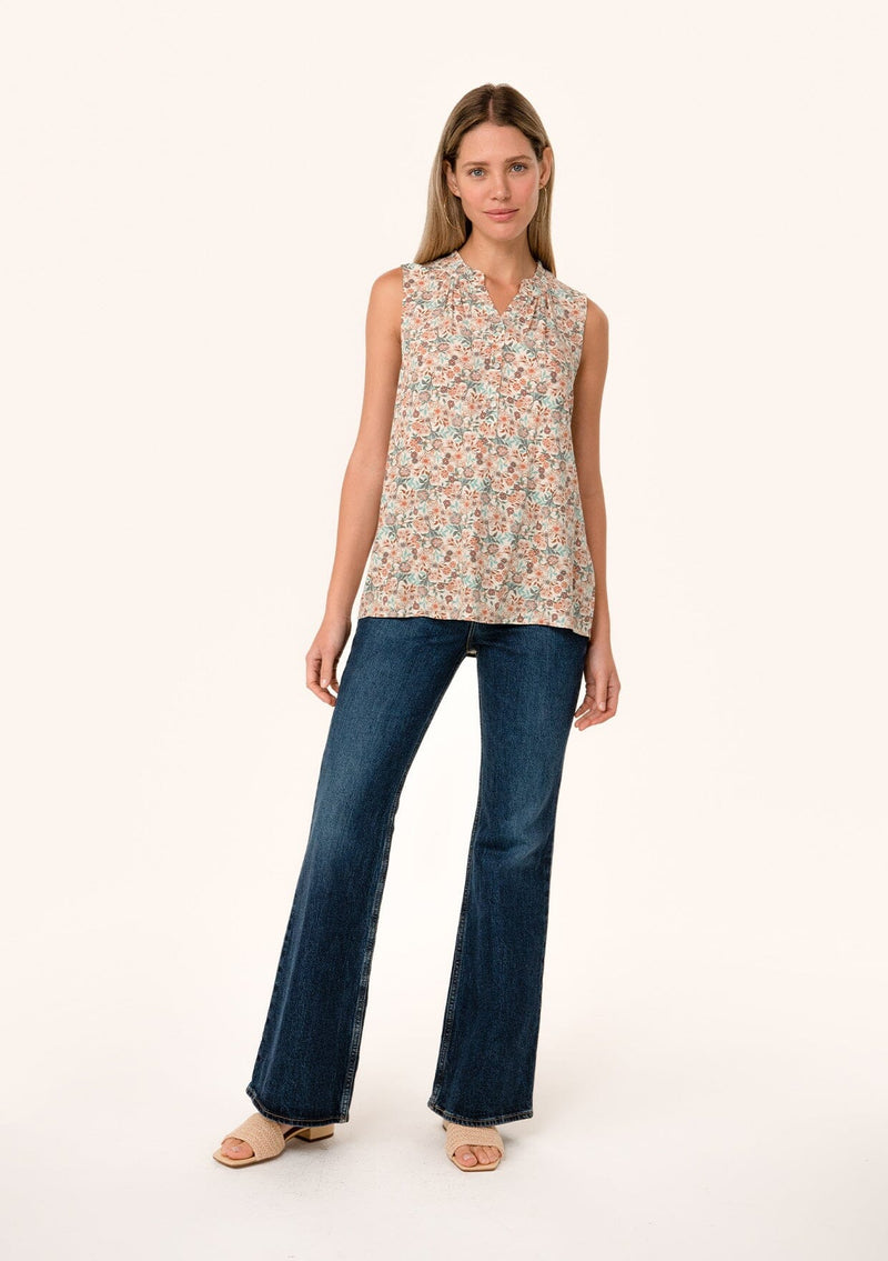 [Color: Cream/Teal] A full body front facing image of a blonde model wearing a transitional fall sleeveless blouse in a cream and teal floral print. With a button front, a ruffle trimmed neckline, and a relaxed fit. 