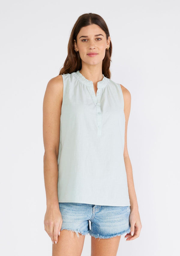 [Color: Dusty Seafoam] A front facing image of a brunette model wearing a sleeveless spring top in dusty seafoam. With a ruffle trimmed round neckline, a button front, and a relaxed fit. 