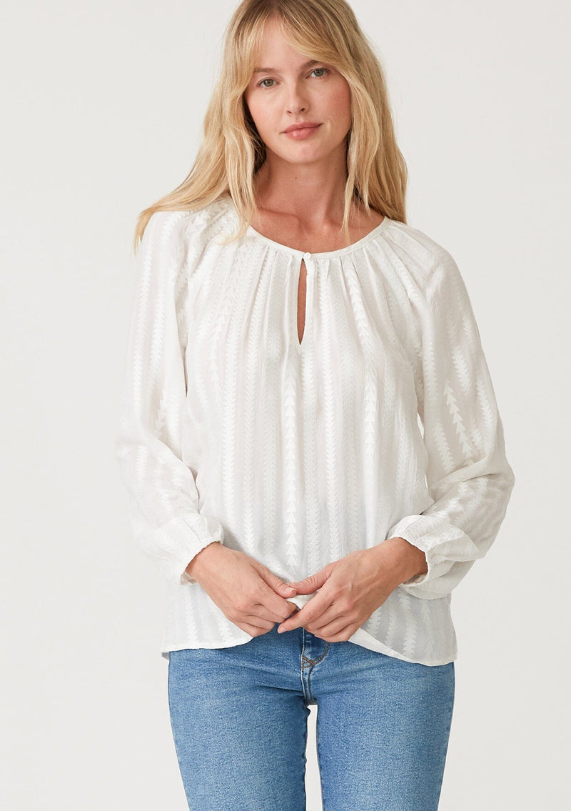 [Color: White] A front facing image of a blonde model wearing a bohemian white blouse with embroidered details. With long raglan sleeves, a round neckline with a single button closure, a front keyhole, and a relaxed fit. 