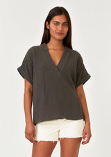[Color: Lagoon] A front facing image of a brunette model wearing an olive green cotton gauze tee. With short cuffed sleeves, a v neckline, and an oversized relaxed fit. 