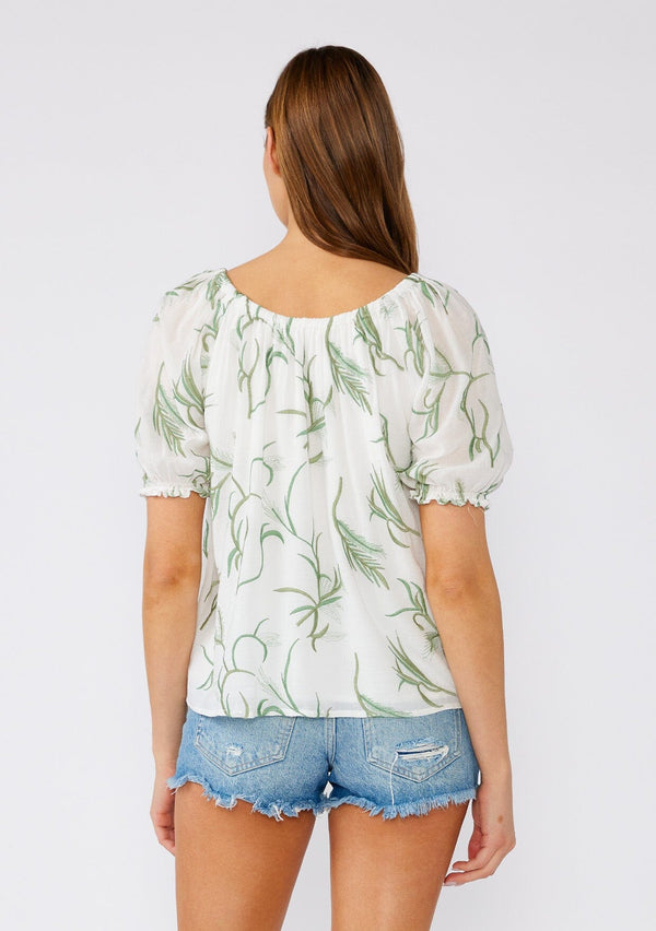 [Color: Off White/Green] A back facing image of a brunette model wearing a bohemian cotton top in a white and green embroidery. With short puff sleeves, a ruffled elastic cuff, an elastic scoop neckline, and a relaxed, flowy fit. 