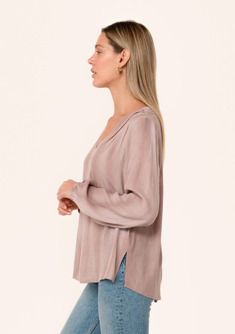 [Color: Rose Water] A side facing image of a blonde model wearing a rose pink bohemian blouse. With long sleeves, a v neckline, and pleated shoulder details. 