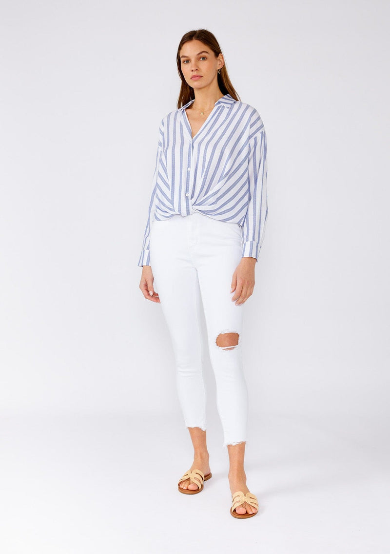 [Color: White/Blue] A full body front facing image of a brunette model wearing a relaxed spring shirt in a white and blue stripe and a metallic gold thread detail. With long sleeves, a dropped shoulder, a v neckline, a collared neckline, a button front, and a knot waist detail. 