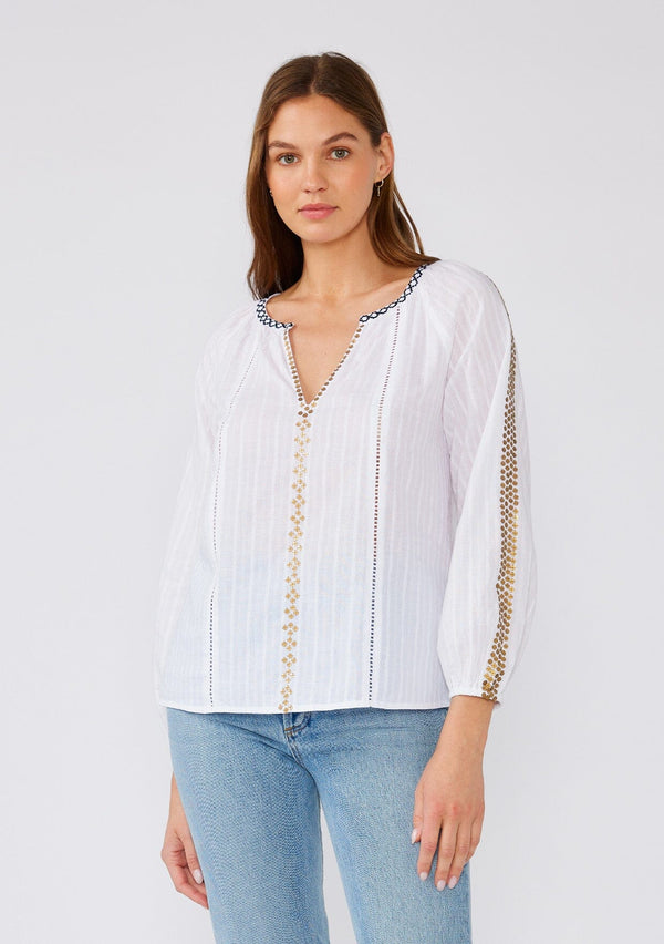 [Color: White/Gold] A front facing image of a brunette model wearing a white cotton bohemian blouse with gold sequined details. With long sleeves, a split v neckline, contrast embroidery, and a relaxed fit. 