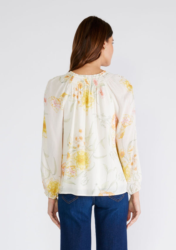 [Color: Vanilla/Coral] A back facing image of a brunette model wearing a beautiful bohemian chic spring blouse in an ivory and coral floral print. With long raglan sleeves, a smocked round neckline, a self covered button front, and a front keyhole. 
