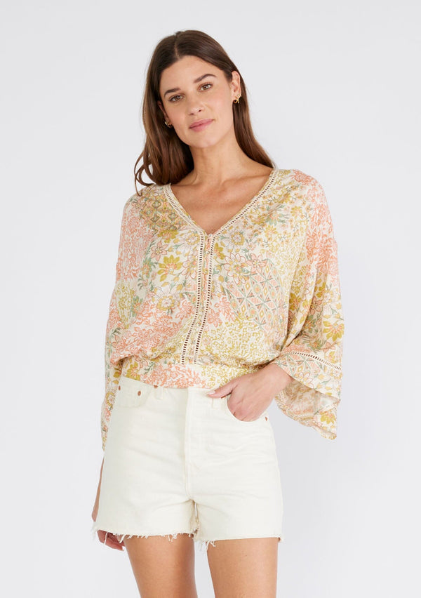 [Color: Dusty Peach/Rust] A front facing image of a brunette model wearing a classic button front bohemian top with dramatic billowy half length sleeves, designed in a peach and rust mixed floral print. With a v neckline, sheer lattice trim, and a slightly cropped length.