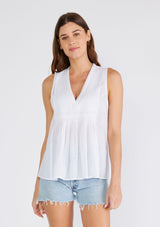 [Color: Chalk] A front facing image of a brunette model wearing a bohemian cotton tank top in a white. With a v neckline, a loose, tent silhouette, and pleated details along the front.