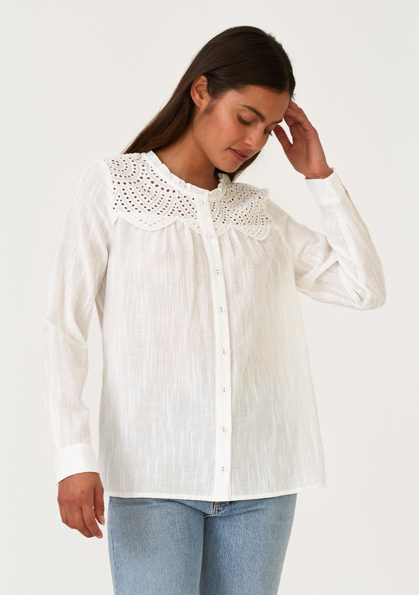[Color: White] A front facing image of a brunette model wearing a white bohemian button front blouse with a ruffled round neckline, a self covered button front, long sleeves, and an eyelet yoke detail. 