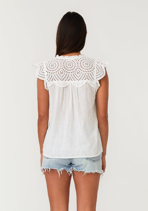 [Color: White] A back facing image of a brunette model wearing a white bohemian spring top with short cap sleeves, a split v neckline, and an eyelet lace yoke. 
