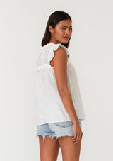 [Color: White] A half body back facing image of a brunette model wearing a white bohemian spring top with short cap sleeves, a split v neckline, and an eyelet lace yoke. 