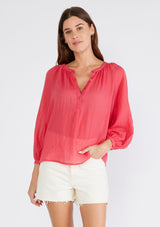 [Color: Coral] A front facing image of a brunette model wearing a red sheer bohemian blouse with long raglan sleeves, a round neckline, a button front, and a relaxed fit. 