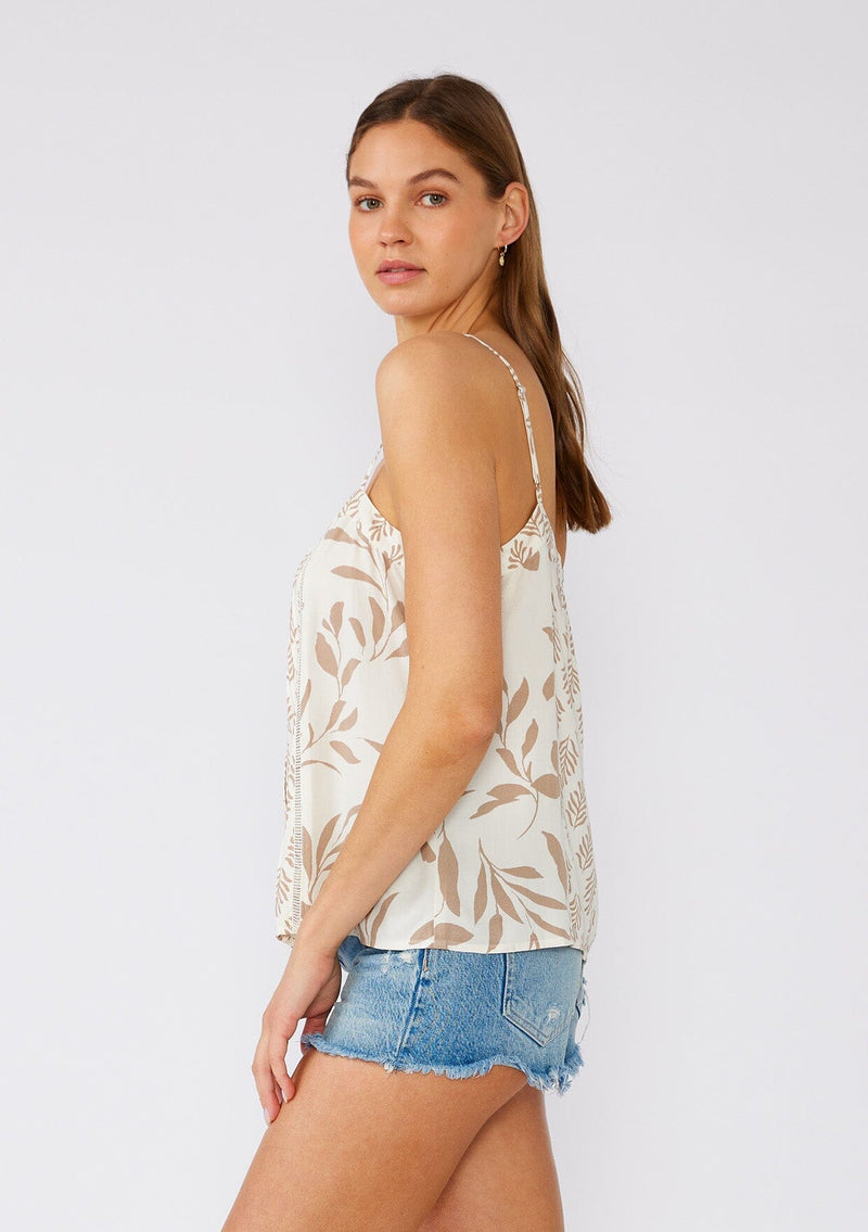 [Color: Latte/Natural] A side facing image of a brunette model wearing a pretty camisole tank top designed in an ivory and brown bohemian print. With adjustable spaghetti straps, a scooped neckline, a self covered button front, lattice trim, a relaxed fit, and pintuck details. 