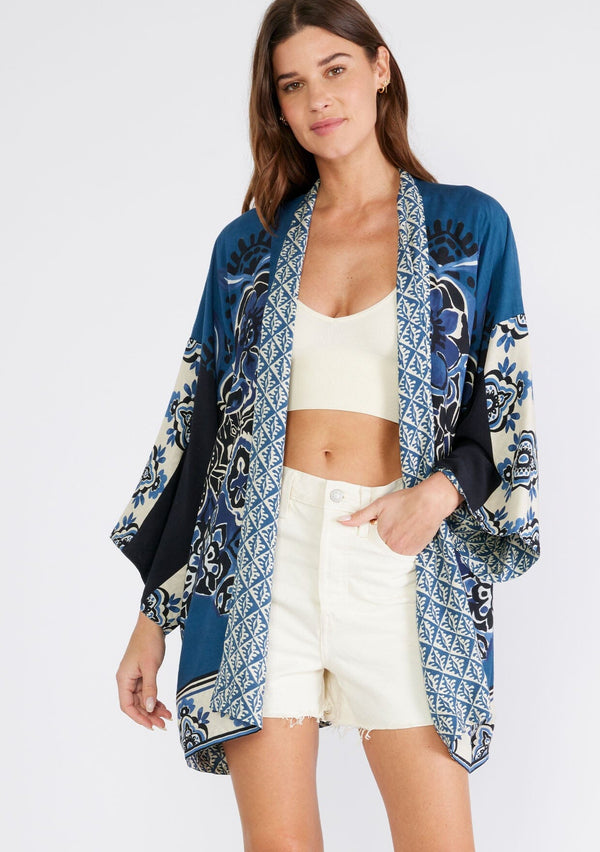 [Color: Indigo/Blue] A front facing image of a brunette model wearing a bohemian kimono in an indigo blue print. With three quarter length long sleeves, an open front, and a mid length. A reversible cover up for the beach or pool side. 