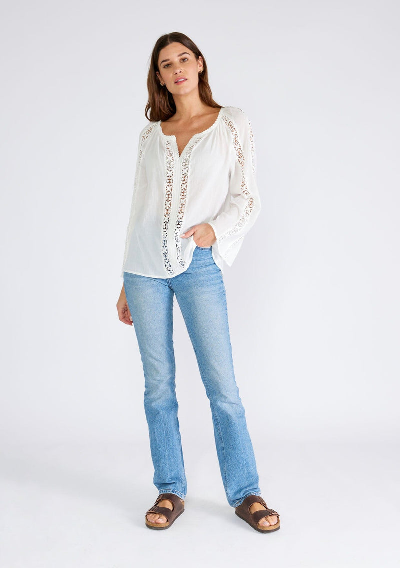 [Color: White] A full body front facing image of a brunette model wearing a classic bohemian white cotton blouse. With crochet trim, a split v neckline, and long bell sleeves. 