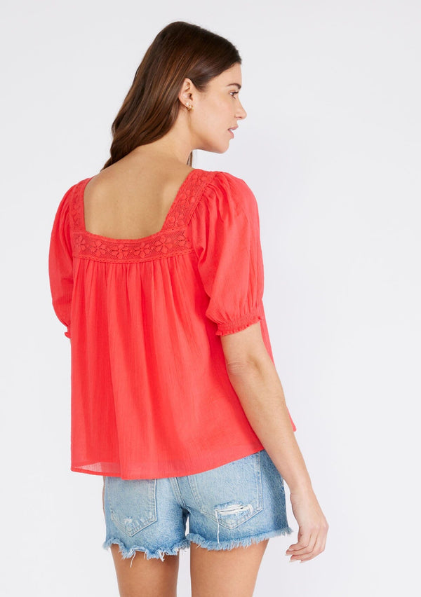 [Color: Hibiscus] A back facing image of a brunette model wearing a bright red cotton bohemian top with short puff sleeved, a ruffled elastic cuff, a square neckline, and lace trim. 
