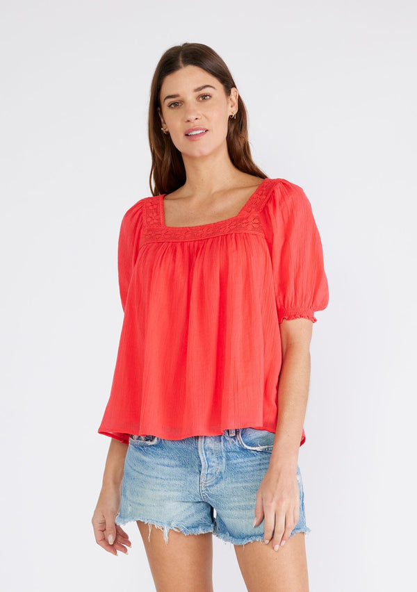 [Color: Hibiscus] A front facing image of a brunette model wearing a bright red cotton bohemian top with short puff sleeved, a ruffled elastic cuff, a square neckline, and lace trim. 