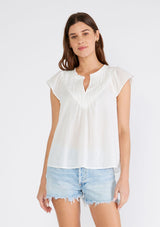 [Color: White] A front facing image of a brunette model wearing a white bohemian top crafted from lightweight cotton gauze. With short cap sleeves, a split v neckline, gathered details at the yoke, and a raw edge hem. 