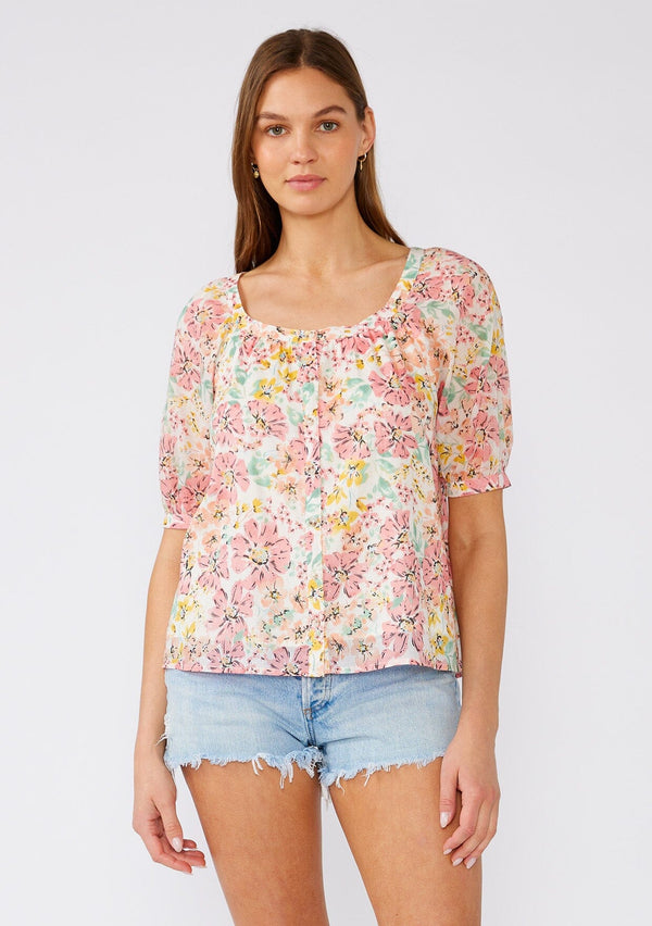 [Color: Natural/Peach Blossom] A front facing image of a brunette model wearing a pink floral cotton summer blouse. With short puff sleeves, a scooped neckline, and a button front. 