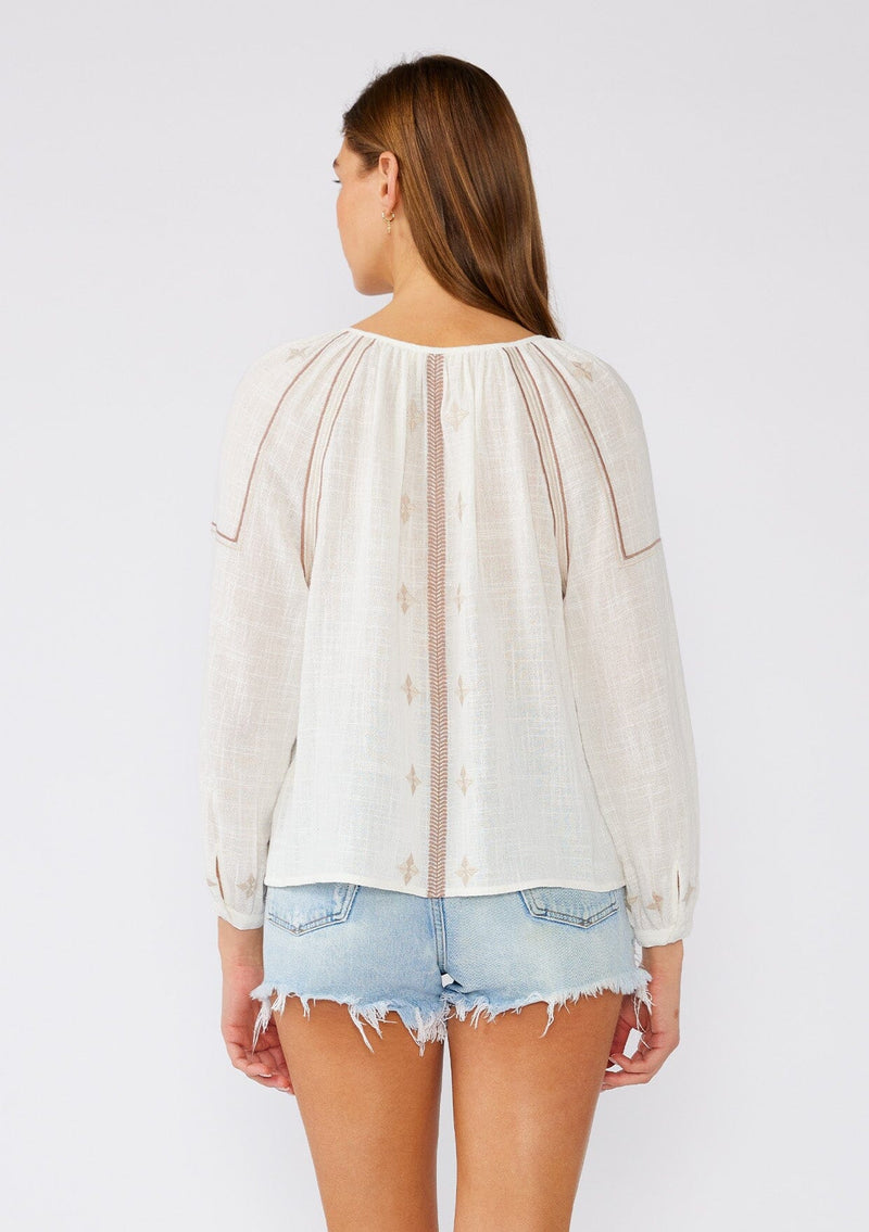 [Color: White/Taupe] A back facing image of a brunette model wearing a white cotton bohemian blouse with taupe brown embroidered details. With long sleeves, a round neckline, a button front, and a relaxed fit. 