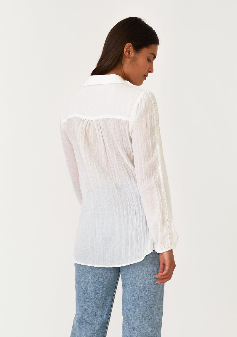 [Color: White] A back facing image of a brunette model wearing a sheer white bohemian shirt. With long sleeves, a collared neckline, a self covered button front, and lace trim. 