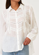 [Color: White] A close up front facing image of a brunette model wearing a sheer white bohemian shirt. With long sleeves, a collared neckline, a self covered button front, and lace trim. 