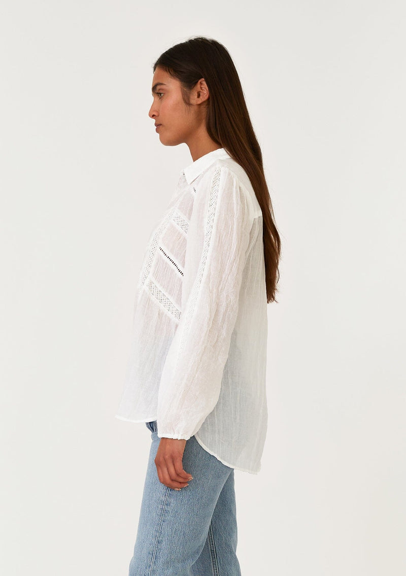 [Color: White] A side facing image of a brunette model wearing a sheer white bohemian shirt. With long sleeves, a collared neckline, a self covered button front, and lace trim. 