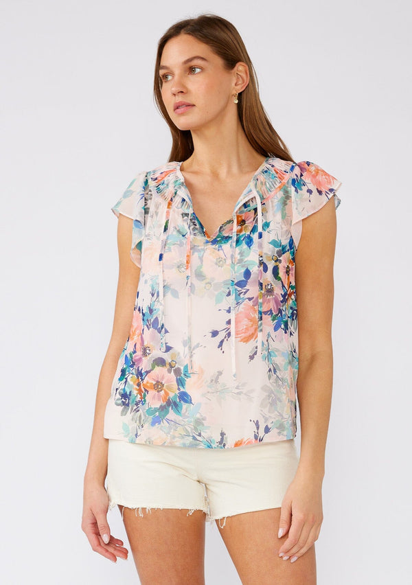 [Color: Peach/Teal] A front facing image of a brunette model wearing a sheer chiffon top in a pink and blue floral print. With short flutter sleeves, a split v neckline with double ties, and pintuck details along the neckline. 