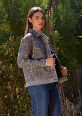 [Color: Wine/Black] A side facing image of a brunette model standing outside wearing a classic bohemian shirt jacket in a black and red patchwork plaid. A fall shirt jacket with long sleeves, a button front, a collared neckline, front patch flap pockets, and side pockets.
