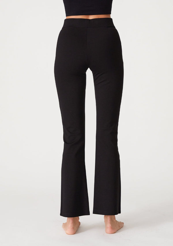[Color: Black] A back facing image of a blonde model wearing a slim fit black flared legging designed in Ponte. With an elastic waist. 