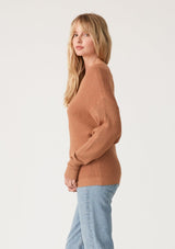 [Color: Clay] A side facing image of a blonde model wearing a clay brown waffle knit pullover sweater. With long sleeves, a relaxed fit, and a wide neckline that can be worn off the shoulder.