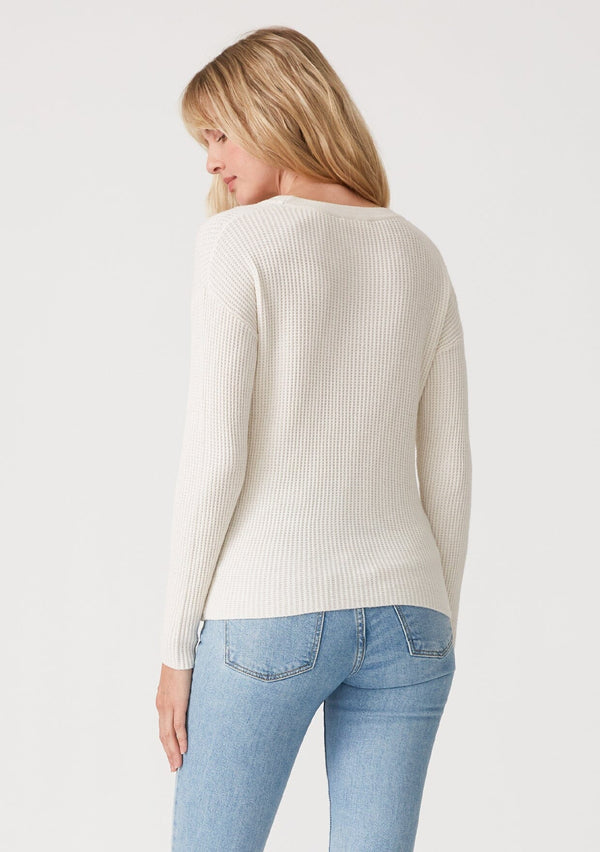 [Color: Natural] A back facing image of a blonde model wearing an ivory waffle knit pullover sweater. With long sleeves, a wide crew neckline, and a twist front detail at the waist. 