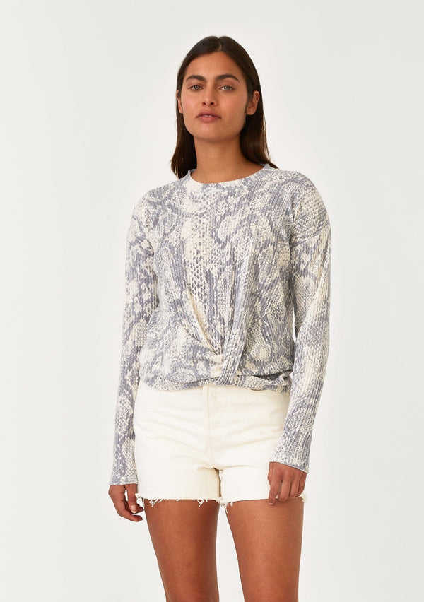 [Color: Light Grey/Ivory] A front facing image of a brunette model wearing a soft waffle knit pullover sweater in a blue grey and ivory snakeskin print. With long sleeves, a crew neckline, and a twist front detail at the waist. 