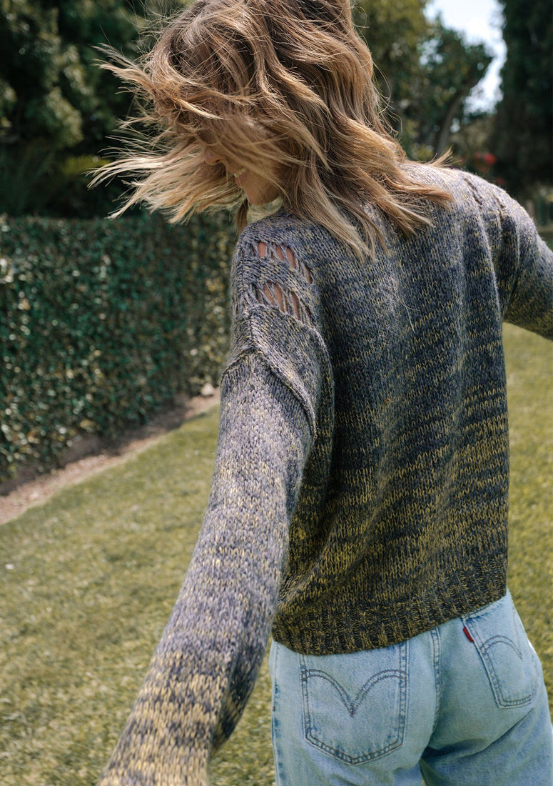 Person wearing a patterned sweater and jeans with a blurred background