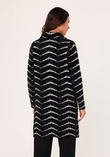 [Color: Black/White] A back facing image of a brunette model wearing a soft and fuzzy sweater coat in a black and white chevron design. With a snap button front, side pockets, and a classic notched lapel.