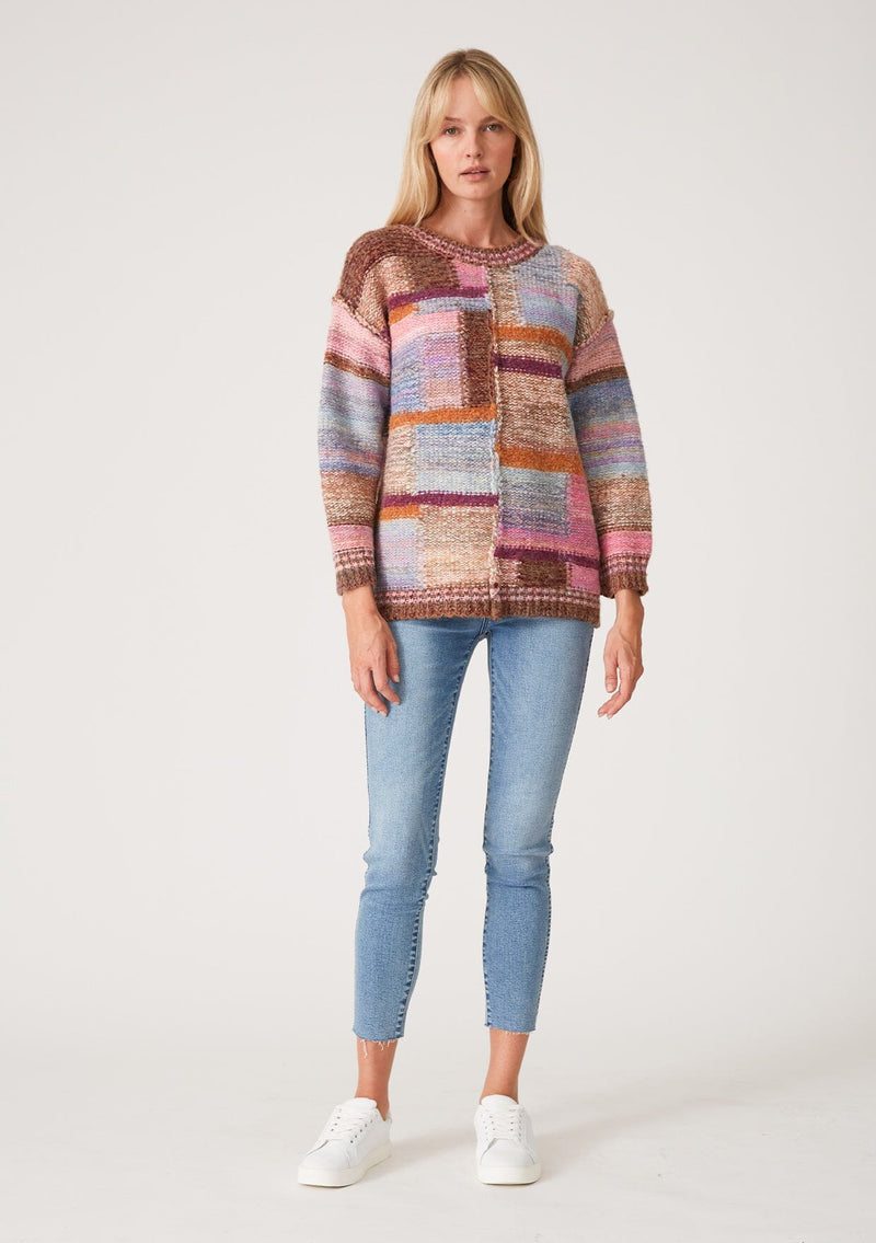 [Color: Pink Multi] A half body front facing image of a red headed model wearing a multi color pink patchwork knit sweater. With long sleeves, a crew neckline, and exposed seam details.