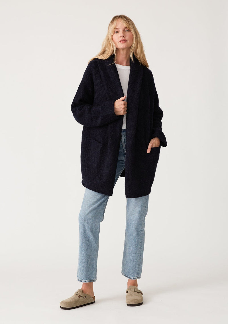 [Color: Navy] A front facing image of a blonde model wearing an oversized sweater coat in navy blue. With an oversized hood, long sleeves, an open front, side pockets, and a mid length. 