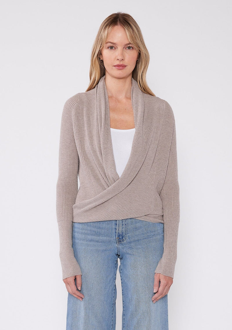 [Color: Heather Cement] A photo of a Lovestitch model wearing a chic beige waffle knit wrap front sweater with long sleeves, a v neckline, and a button closure at the back. The long ties can be styled in multiple ways.