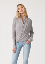 [Color: Heather Grey] A half body front facing image of a blonde model wearing a heather grey waffle knit wrap sweater with long sleeves, a v neckline, and a button closure at the back. The long ties can be styled in multiple ways. 