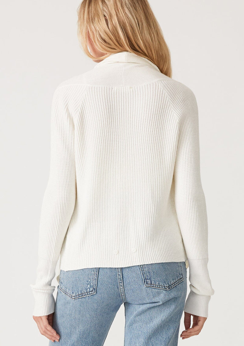 [Color: Ivory] A back facing image of a blonde model wearing an ivory waffle knit wrap sweater with long sleeves, a v neckline, and a button closure at the back. The long ties can be styled in multiple ways. 