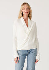 [Color: Ivory] A half body front facing image of a blonde model wearing an ivory waffle knit wrap sweater with long sleeves, a v neckline, and a button closure at the back. The long ties can be styled in multiple ways. 