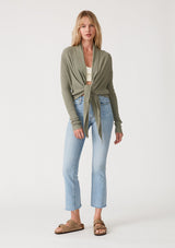 [Color: Olive] A full body front facing image of a blonde model wearing an olive green waffle knit wrap sweater with long sleeves, a v neckline, and a button closure at the back. The long ties can be styled in multiple ways. 