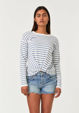 [Color: Ivory/Dusty Blue] A front facing image of a brunette model wearing a classic ivory and light blue striped knit pullover sweater. With long sleeves, a drop shoulder, a crew neckline, and a twist front detail at the waist. 